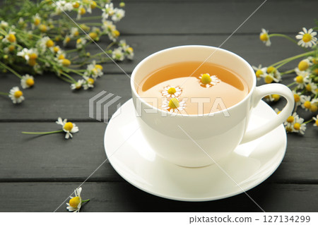 Aromatic herbal tea in white cup and chamomiles on black wooden background. Space for text 127134299