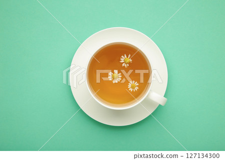 Aromatic herbal tea in white cup and chamomiles on mint background. 127134300