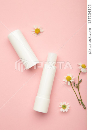 Lip balms and chamomile flowers on pink background. 127134303