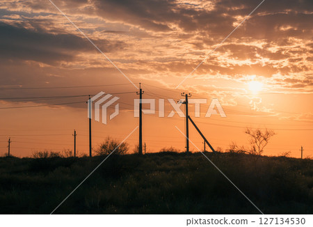 Sunset over rural landscape with power lines silhouetted against golden sky. 127134530