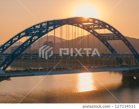 Evening panorama of a blue arch bridge with moving cars over calm water at sunset. Hangzhou, China. 127134531