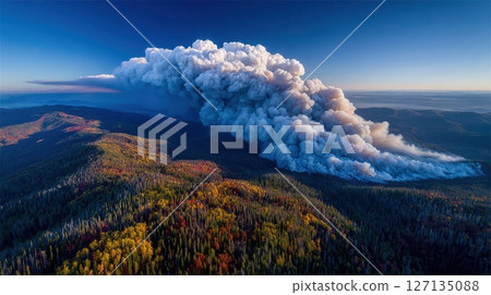An aerial perspective reveals a wildfire's smoke plume billowing above an autumn forest, displaying the environmental impact on nature with a blue sky backdrop An aerial perspective reveals a wildfire's smoke plume billowing above an autumn forest, displaying the environmental impact on nature with a blue sky backdrop 127135088