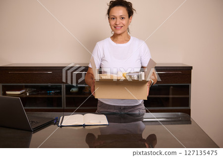 Smiling Woman With a Gift Box in a Home Office Environment 127135475