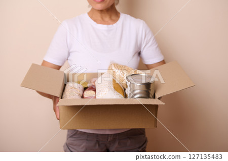 Person Holding a Box Containing Non-Perishable Food Supplies for Donation or Charity 127135483