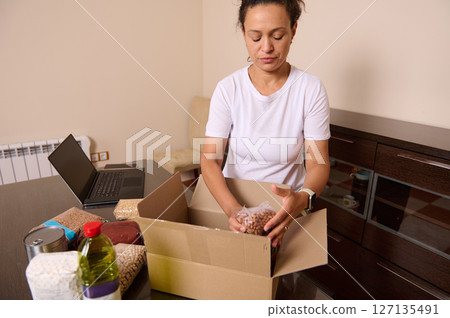Woman Packing Food in a Box at Home for Charity Donation or Food Bank Arrival 127135491