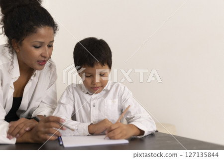 Teacher helping young pupil with writing exercise at school desk Teacher helping young pupil with writing exercise at school desk 127135844