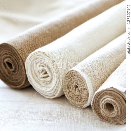 Rolls of linen fabric in various neutral tones arranged on table, background 127137145