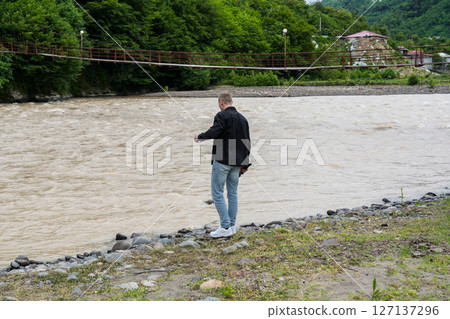 A man stands by a river in the mountains of Georgia 127137296