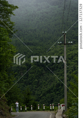 Road down, power line pole and mountain view, cloudy 127137329