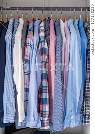 Neatly arranged men shirts hanging on wooden hangers in wardrobe. Minimalist clothing organization and classic male fashion concept 127138239