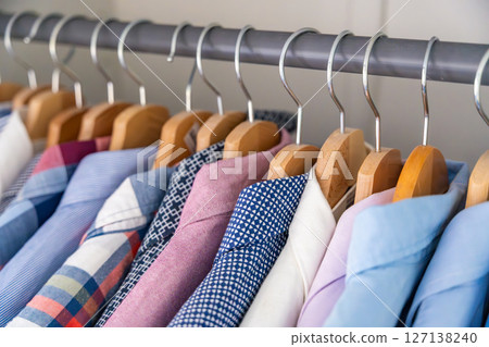 Neatly arranged men shirts hanging on wooden hangers in wardrobe. Minimalist clothing organization and classic male fashion concept Neatly arranged men shirts hanging on wooden hangers in wardrobe. Minimalist clothing organization and classic male fashion concept 127138240