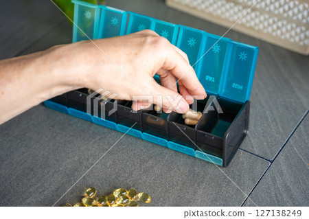 Close up view of Man hand sorting his pills and supplements into a weekly pill organizer. Concept of medication management and daily health routine Close up view of Man hand sorting his pills and supplements into a weekly pill organizer. Concept of medication management and daily health routine 127138249
