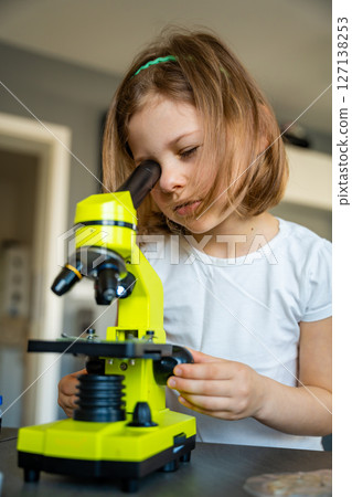 Little girl looking through a green microscope. Concept of curiosity and early scientific exploration 127138253
