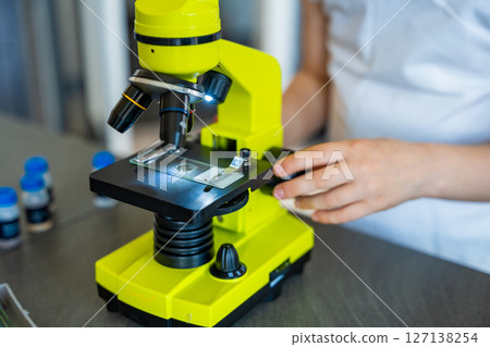 Close up view of hands of little girl preparing a sample for microscope examination. Concept of hands-on science learning and curiosity-driven exploration 127138254