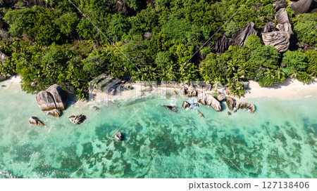 Turquoise waters of the shoreline with rocky formations surrounded by lush greenery. La Digue, Seychelles. 127138406
