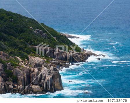 Granite cliffs border the ocean with turquoise waves splashing. Seychelles, Felicite. Granite cliffs border the ocean with turquoise waves splashing. Seychelles, Felicite. 127138476