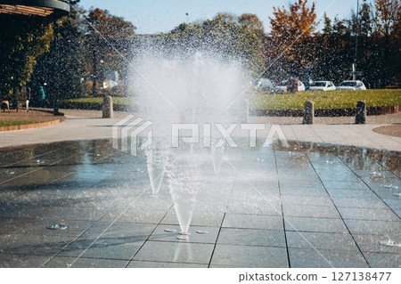 Water droplets spread from the fountain in the air. Splashing water from a fountain in the park. Vertical fountain jets in the sidewalk on the square in the city park. Water droplets spread from the fountain in the air. Splashing water from a fountain in the park. Vertical fountain jets in the sidewalk on the square in the city park. 127138477