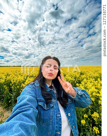 Carefree female tourist taking smartphone selfie in spectacular yellow flower field. Rapeseed flowers. Great for social media aesthetics, positivity campaigns, and springtime visuals. 127138771