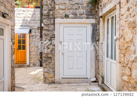 White doors and stone walls in a quiet Mediterranean courtyard. Architecture, tradition, and rustic European living. 127139082