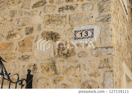 House number 13 on stone wall facade. Mediterranean style, decorative tile, urban detail, and street numbering. 127139111