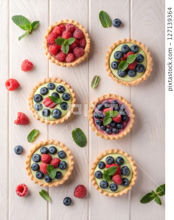 Assorted berry tarts with mint leaves on white wooden background, top view. 127139364
