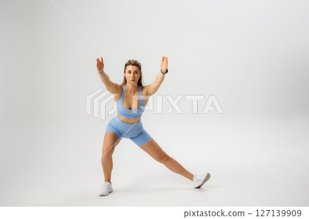 Fitness model performing a dynamic side lunge exercise in a studio setting during a fitness session 127139909