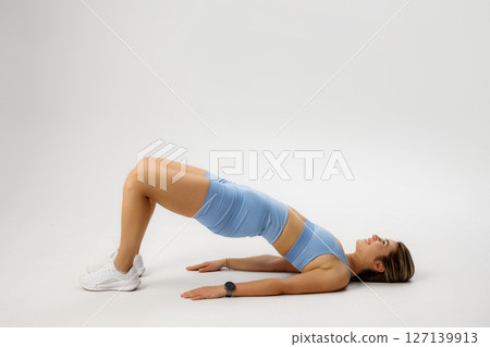 Fitness enthusiast performs a bridge exercise in a minimalist indoor setting during a workout session focused on core strength 127139913