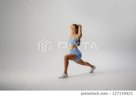 Female athlete performing a forward lunge in a light blue workout set on a neutral background Female athlete performing a forward lunge in a light blue workout set on a neutral background 127139925