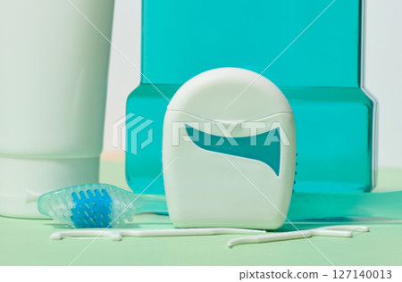 Various dental hygiene products, including dental floss, toothbrush, and mouthwash, are displayed on a light green surface 127140013