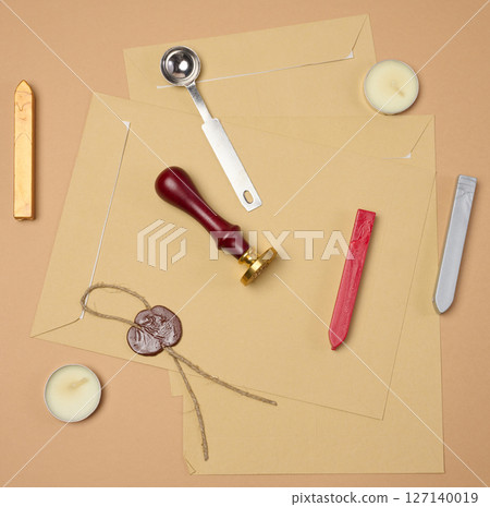 A wax seal kit including wax sticks, spoon, candles, stamp and sealed scroll placed on a neutral background 127140019