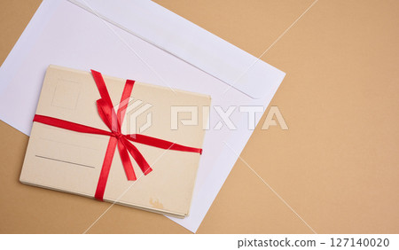 A stack of blank postcards tied with a red ribbon with a bow and an envelope lie on a beige background. 127140020