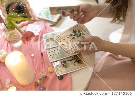 Feminine hands holding tarot cards above a pink-toned ritual table with candles, symbolizing spirituality, intuition, and inner connection. 127140106