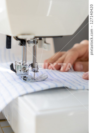 woman sews a light fabric on a sewing machine. making clothes, hobbies. woman sews a light fabric on a sewing machine. making clothes, hobbies. 127140420