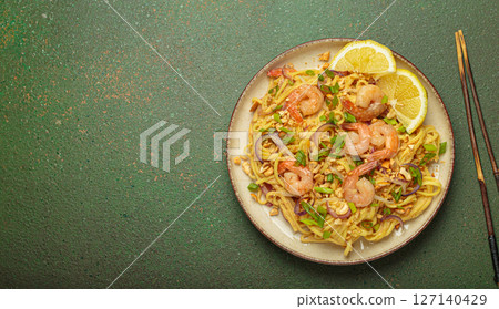 Pad thai noodles with shrimps and chopsticks on rustic green background, traditional dish of Thailand, space for text 127140429