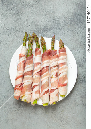 Fresh asparagus wrapped in bacon with peppercorns on gray concrete background top view Fresh asparagus wrapped in bacon with peppercorns on gray concrete background top view 127140434