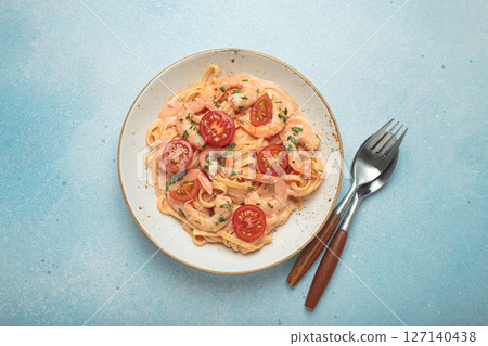 Seafood pasta linguine with shrimps and cherry tomatoes in creamy sauce garnished with parsley on white plate on light blue background top view Seafood pasta linguine with shrimps and cherry tomatoes in creamy sauce garnished with parsley on white plate on light blue background top view 127140438