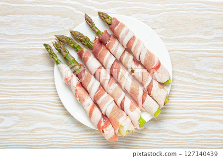 Fresh asparagus wrapped in bacon with peppercorns on white wooden table top view Fresh asparagus wrapped in bacon with peppercorns on white wooden table top view 127140439
