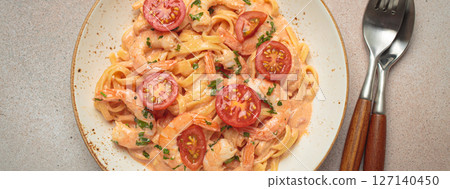 Seafood pasta linguine with shrimps and cherry tomatoes in creamy sauce garnished with parsley on white plate on light warm beige background top view 127140450