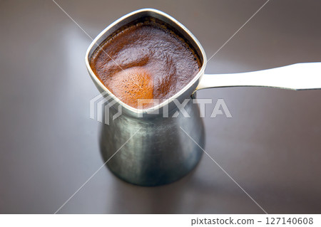Minimalist shot of a silver cezve holding rich Turkish coffee on a gray surface Minimalist shot of a silver cezve holding rich Turkish coffee on a gray surface 127140608