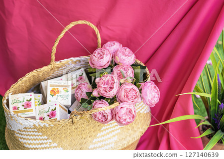 Wicker basket filled with natural cosmetic boxes with creams and roses, bright pink fabric background. Concept of natural skin care, eco and floral inspiration. Rosa damascena. Rose production season 127140639
