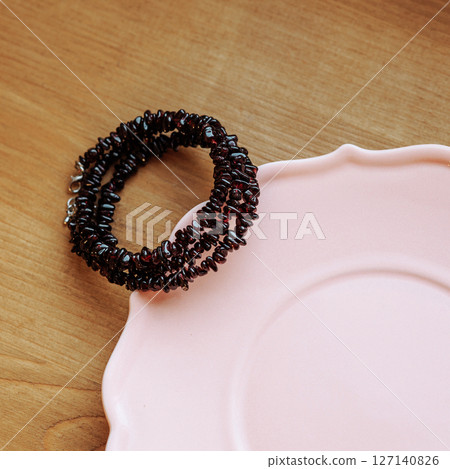 Dark red garnet chip bracelet on pink ceramic plate with wooden background Dark red garnet chip bracelet on pink ceramic plate with wooden background 127140826