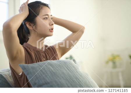 A woman in her 20s with a troubled face sitting on a sofa 127141185