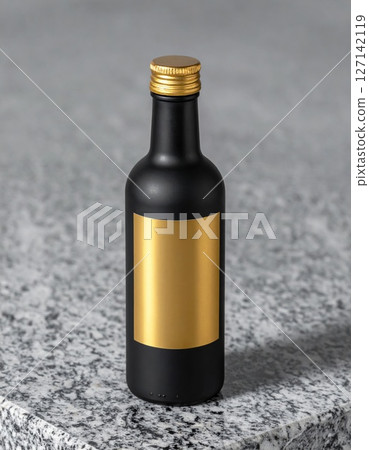 Black Mini Bottle with Gold Label on Grey Surface 127142119