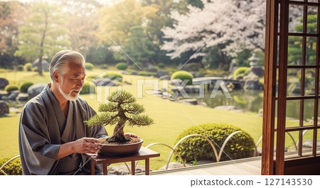 A senior man with a calm expression admiring his bonsai on a veranda bathed in sunlight 127143530