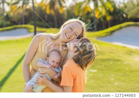 Mother, older son, and newborn baby on a meadow in the park. Family spending quality time together in nature. Parenthood, love, and family bond concept Mother, older son, and newborn baby on a meadow in the park. Family spending quality time together in nature. Parenthood, love, and family bond concept 127144003