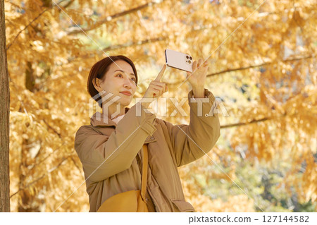 Middle-aged woman taking video of autumn leaves with her smartphone Middle-aged woman taking video of autumn leaves with her smartphone 127144582