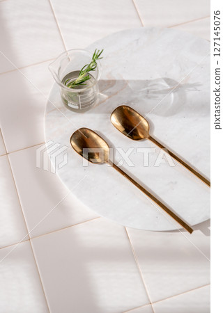 An elegant composition of glass and golden spoons on a white background An elegant composition of glass and golden spoons on a white background 127145076