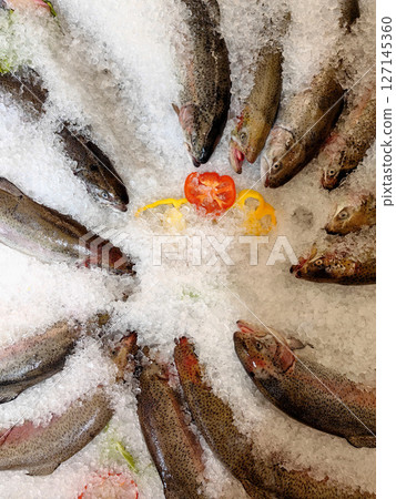 freshly chilled trout arranged on ice with colorful vegetables for seafood market. closeup. 127145360
