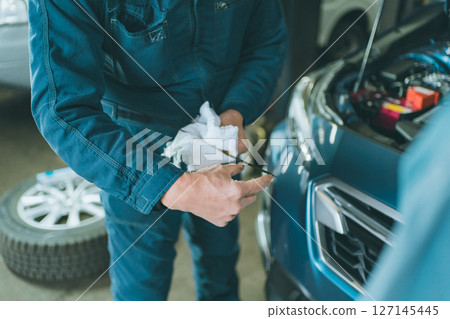 Auto mechanic checking engine oil at an auto repair shop Auto mechanic checking engine oil at an auto repair shop 127145445