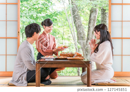 A female inn staff member explaining the dishes in a guest room at a hot spring inn 127145851